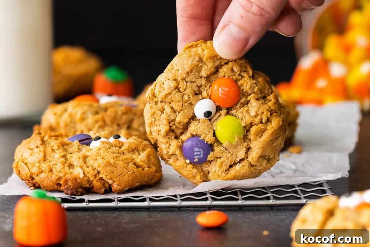 Spooky Halloween Monster Cookie Recipe for Party Treats 3 Hand holding up a halloween monster cookie to show the colorful candies on top.