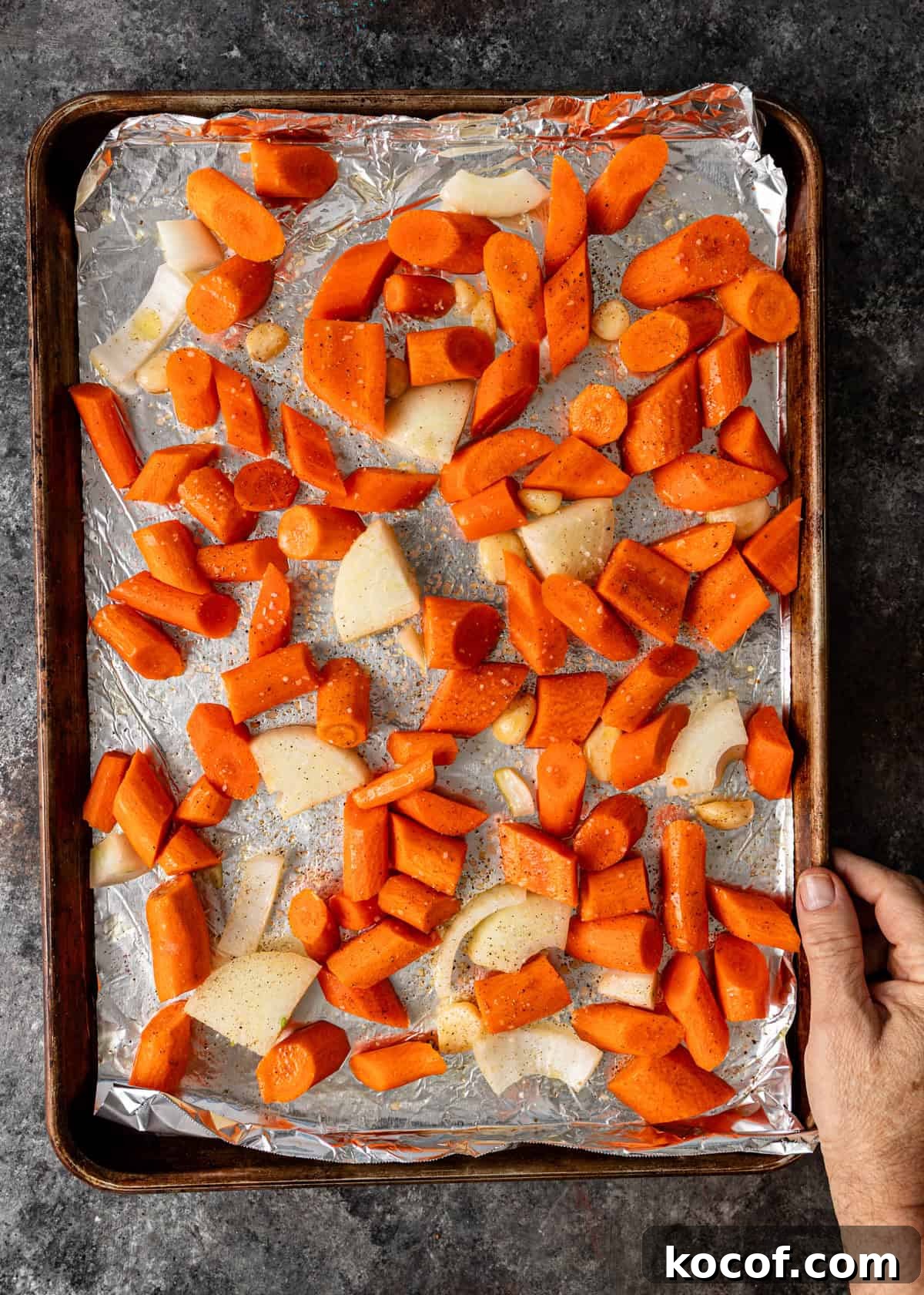 Roasted Carrot and Goat Cheese Dip Recipe for Entertaining 4 overhead process shot: hand holding sheet pan with chopped carrots and onions on foil