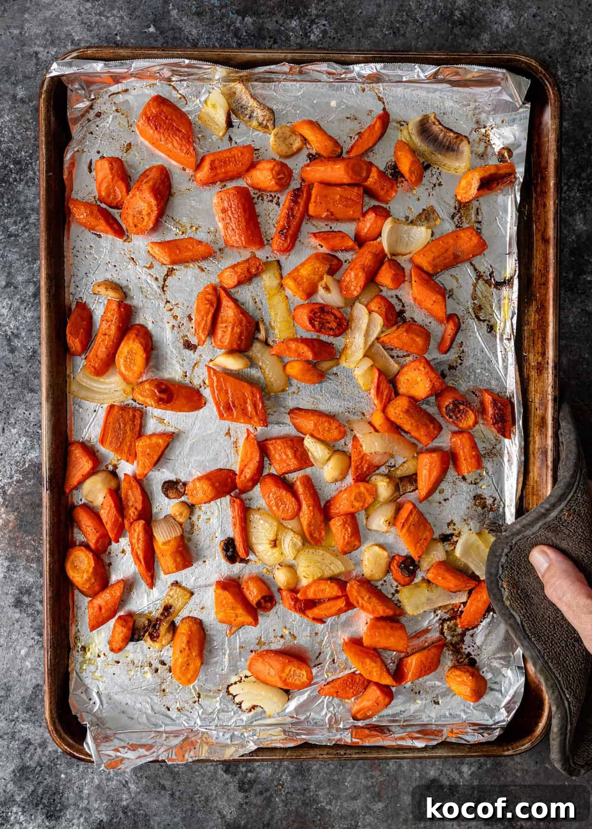 Roasted Carrot and Goat Cheese Dip Recipe for Entertaining 5 overhead process shot: hand holding hot pad holding a sheet pan with cooked chopped carrots and onions on foil