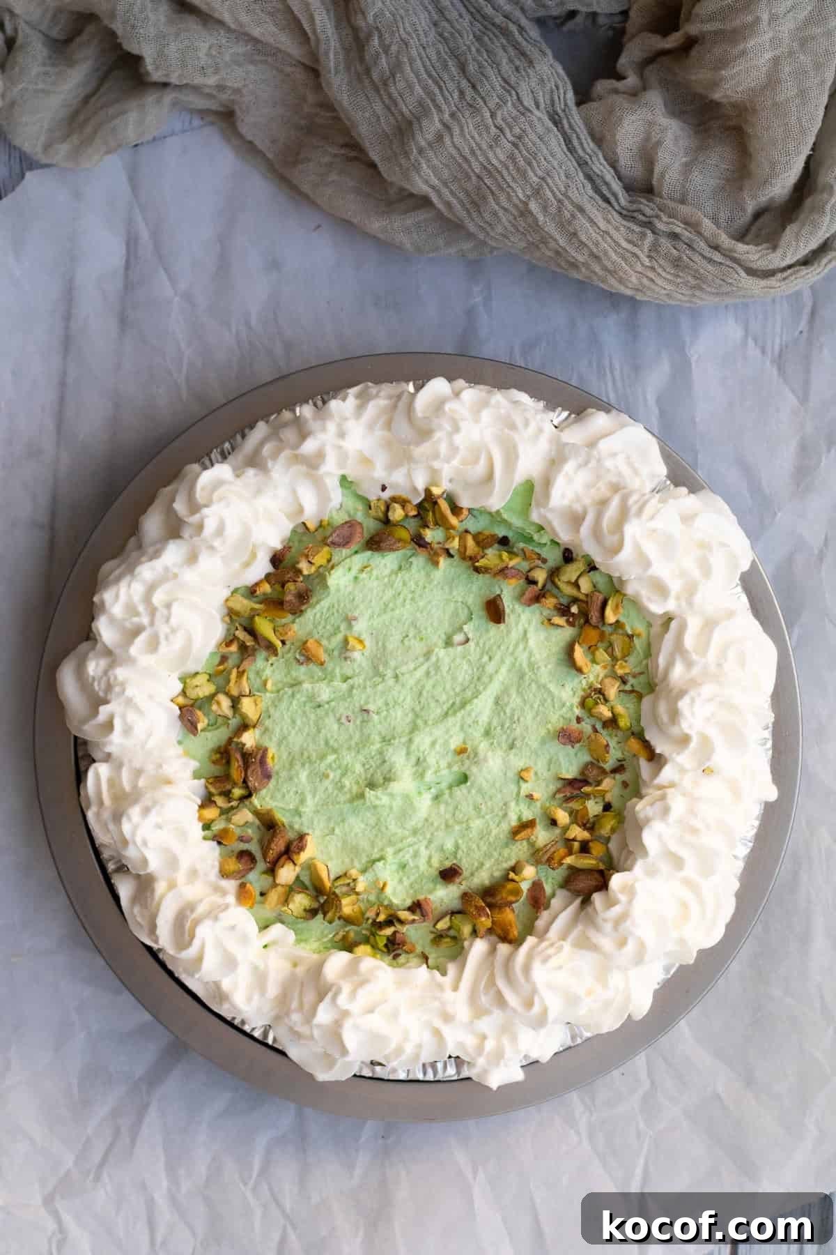 pistachio pie in a tin garnished with whipped cream and chopped pistachios