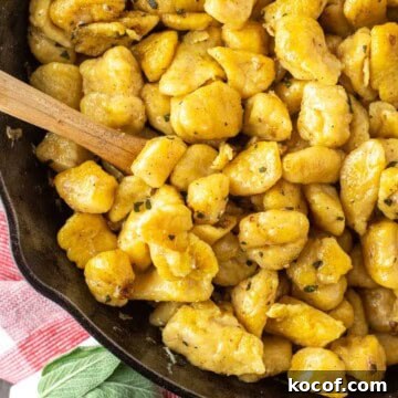 Spoon dipped in butternut squash gnocchi in skillet.