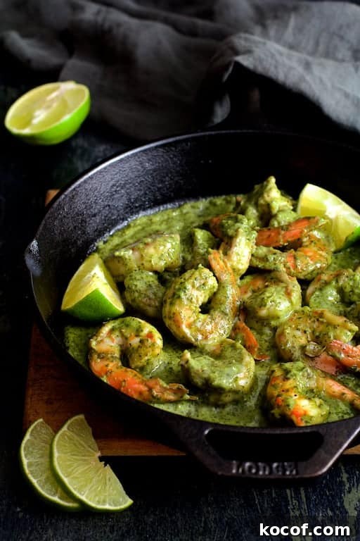 Garlic Butter Shrimp Served in Creamy Avocado Halves 2 Photo of Shrimp in Avocado Butter in cast iron skillet garnished with lime wedges on wood trivet.
