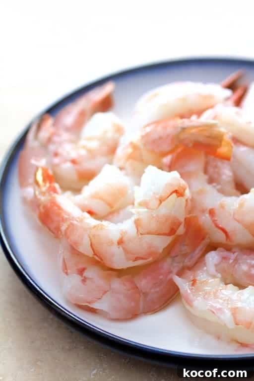 Garlic Butter Shrimp Served in Creamy Avocado Halves 5 Photo of fresh, uncooked shrimp on white plate with blue rim.
