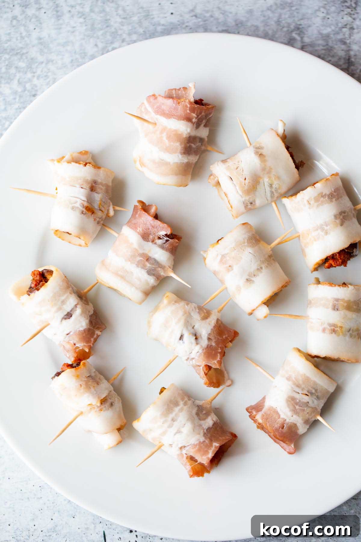 Crispy Air Fryer Stuffed Dates with Goat Cheese & Bacon 5 Uncooked bacon wrapped dates on a plate.