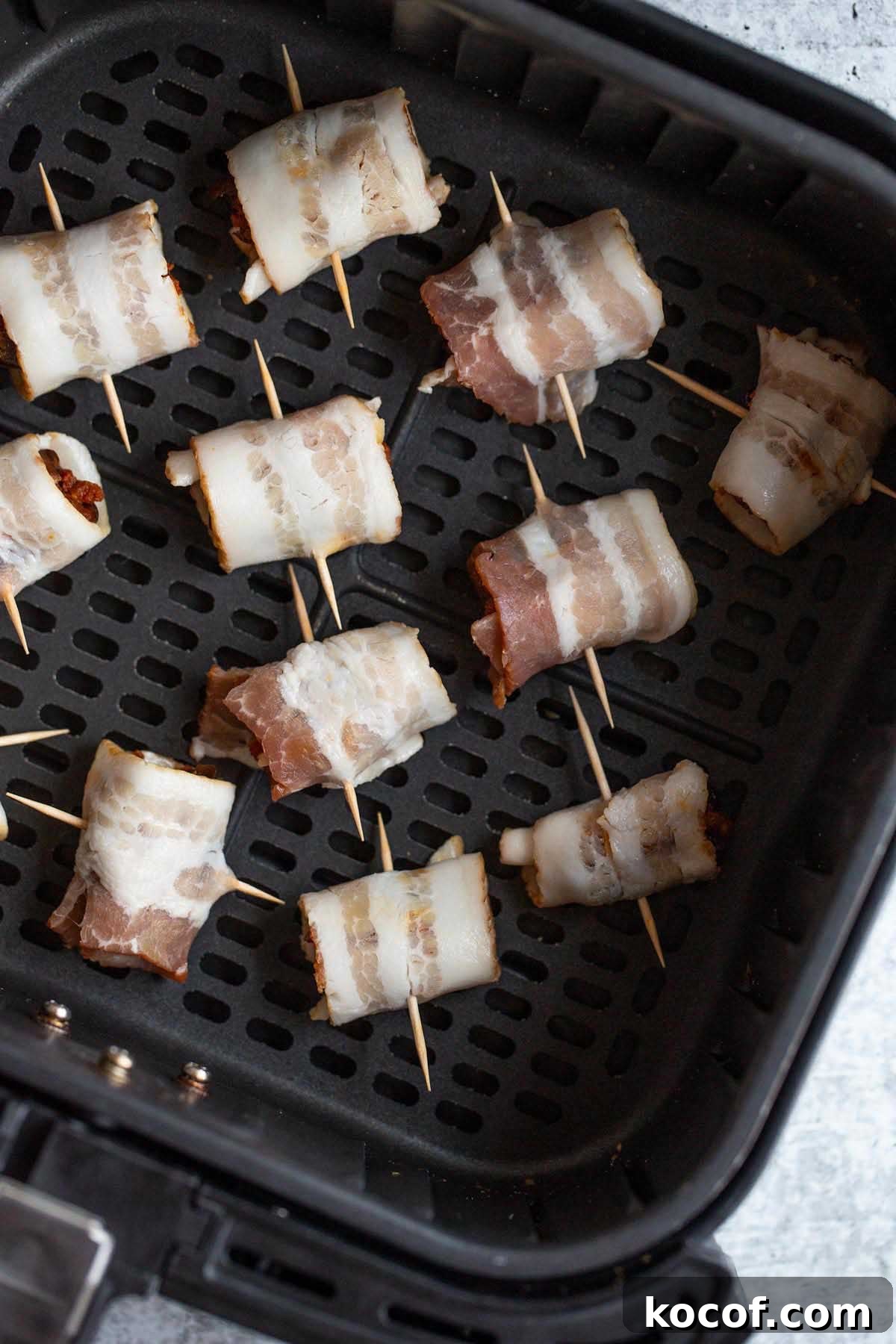 Crispy Air Fryer Stuffed Dates with Goat Cheese & Bacon 6 Uncooked bacon wrapped dates in air fryer basket.