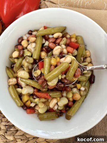 A bowl of green bean salad with a serving spoon, a napkin on the side and peppers near the bowl.