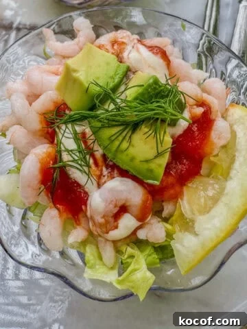 A small bowl of shrimp cocktail with lettuce, lemon, celery and avocado.