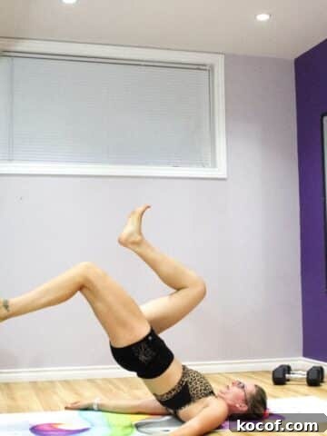 Woman performing a single leg glute bridge with one foot on a bench.