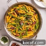A close-up shot of a skillet with bacon and asparagus pasta garnished with fresh tarragon.