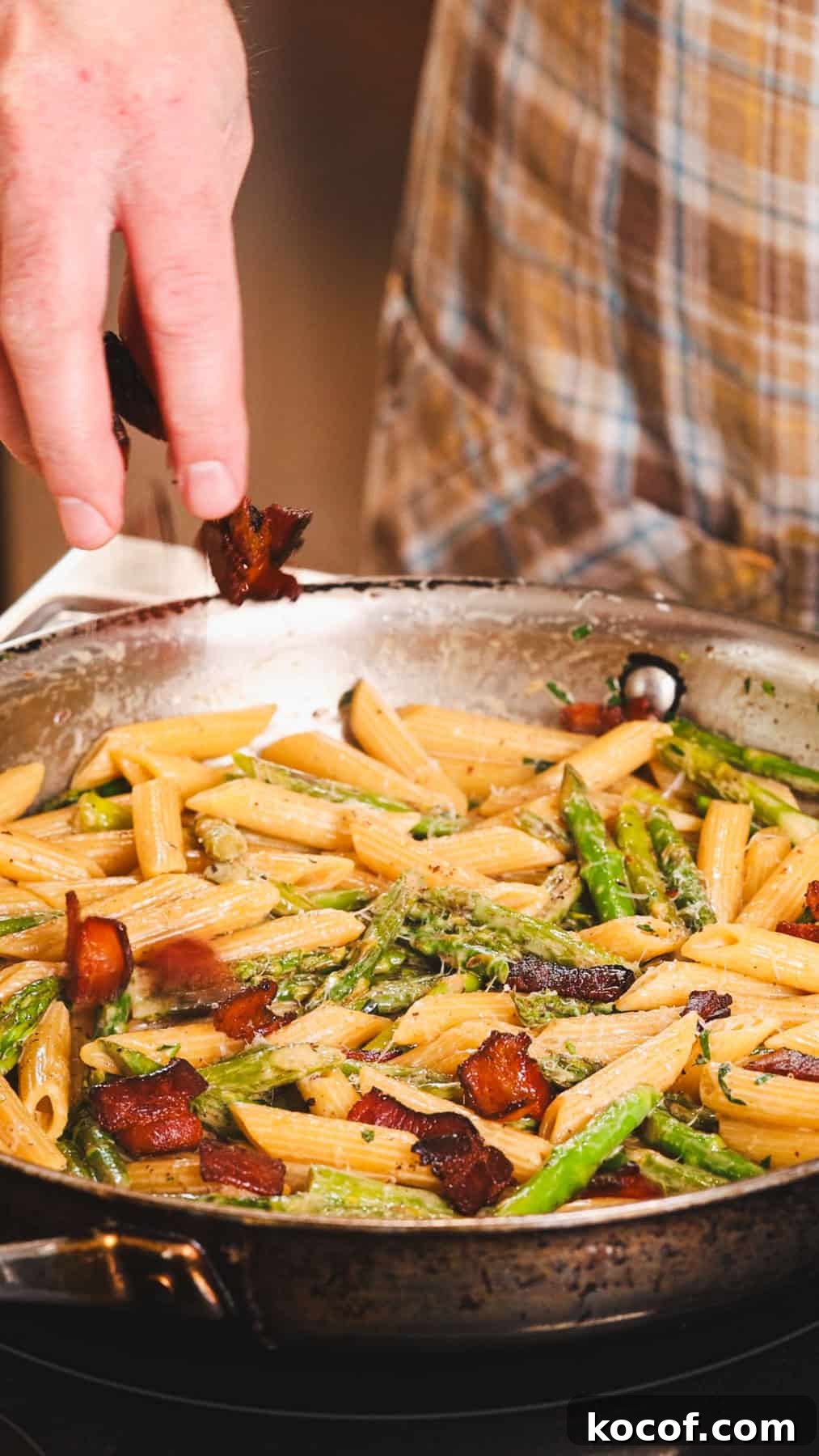 Creamy Bacon and Asparagus Pasta Recipe for Spring Meals 7 Crispy cooked bacon getting sprinkled into a skillet with pasta and asparagus and a light cream sauce.