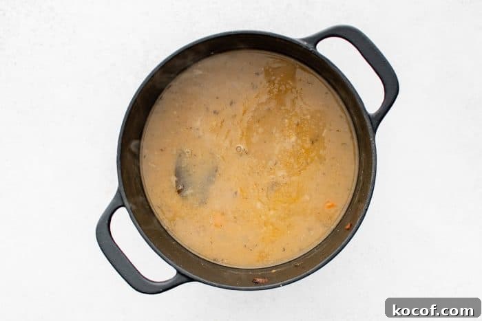 Overhead view of a black Dutch oven filled with a simmered, tan, gravy-like pork stew broth, lightly steaming.