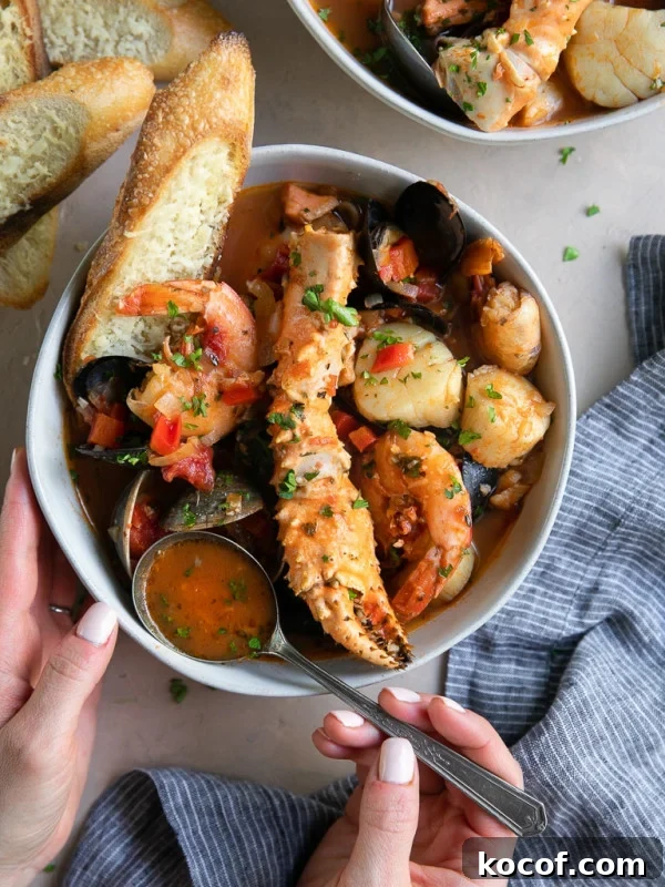 A bowl Cioppino seafood stew filled with shrimp, scallops, crab legs, fish, clams, and mussels and served with slices of bread.