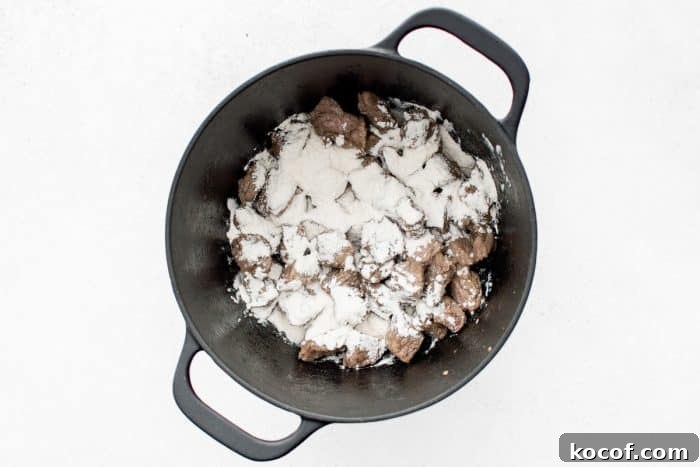 Overhead view of browned pork chunks in a black Dutch oven dusted with a thick layer of white all-purpose flour.
