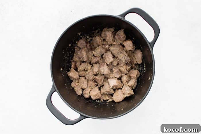 Overhead view of flour-coated pork stew meat in a black Dutch oven, with the flour absorbed and clinging to the pork.
