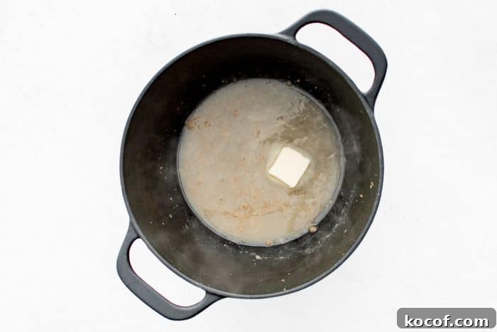Overhead view of a black Dutch oven with pale deglazing liquid and a pat of butter melting.