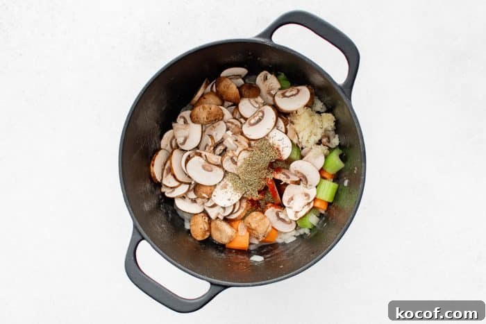 Overhead view of a black Dutch oven filled with sautéed vegetables topped with sliced mushrooms, garlic, thyme, and paprika.