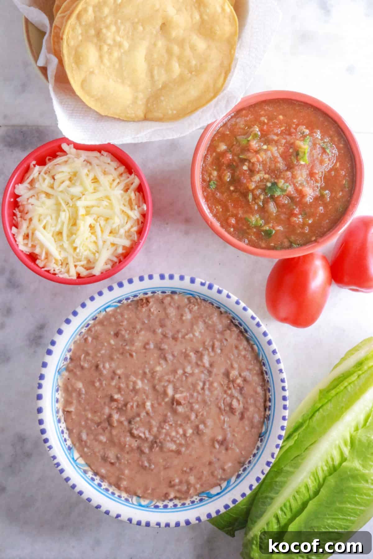 Refried Bean Tostadas with Crispy Tortillas and Fresh Salsa 3 Corn tostadas, a bowl with shredded cheese, a bowl with jalapeño salsa, a bowl with refried beans, 2 roma tomatoes and lettuce