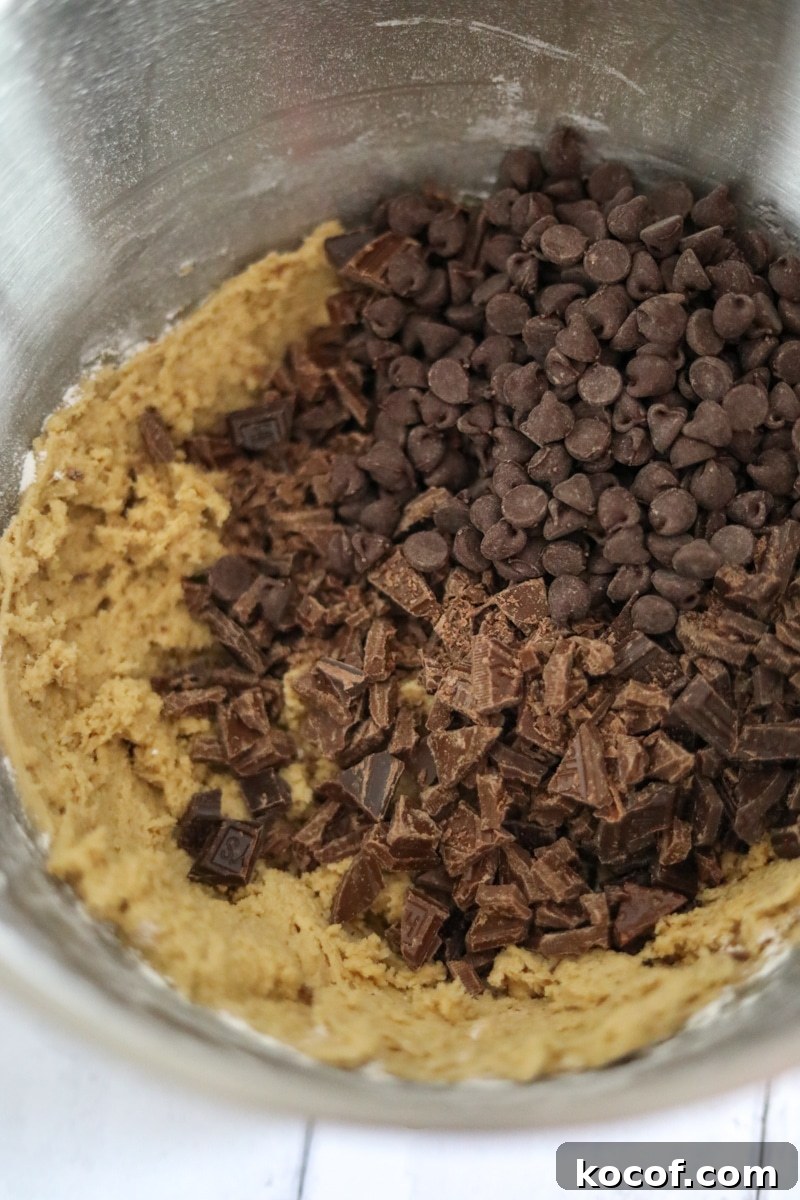 3 kinds of chocolate chip cookies being added to the batter in a metal bowl