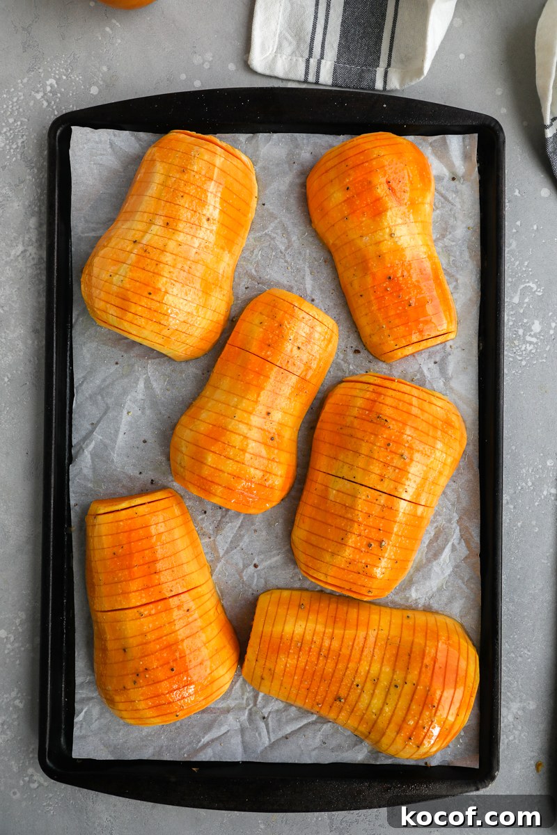 Honeynut squash cut hasselback style on a baking sheet with parchment paper