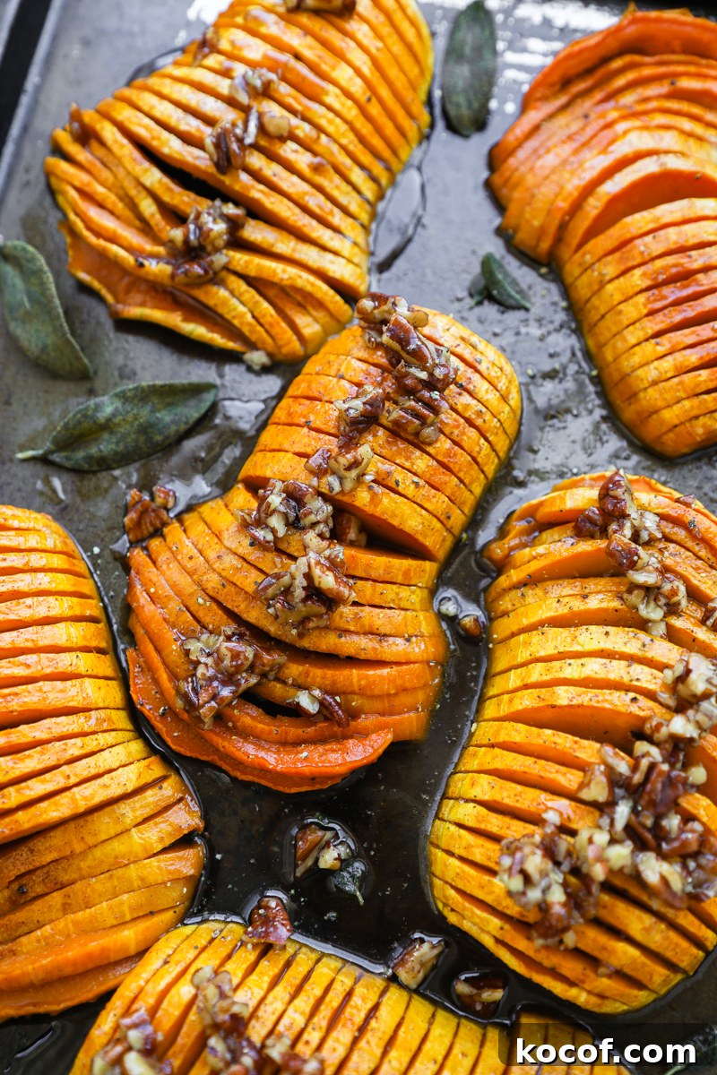 Multiple sweet squash halves on a baking sheet with crispy sage leaves and a rich pecan sauce on top