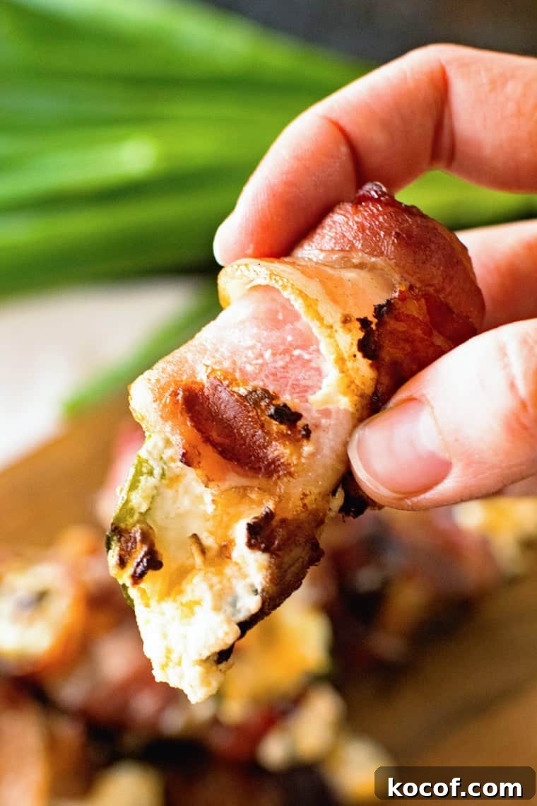 Bacon-Wrapped Jalapeño Poppers: Baked or Grilled Recipes 2 Hand holding grilled bacon wrapped jalapeno popper with cream cheese filling