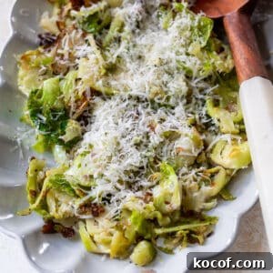 shaved brussels sprouts topped with shredded cheese next to a wooden spoon on a white serving platter.