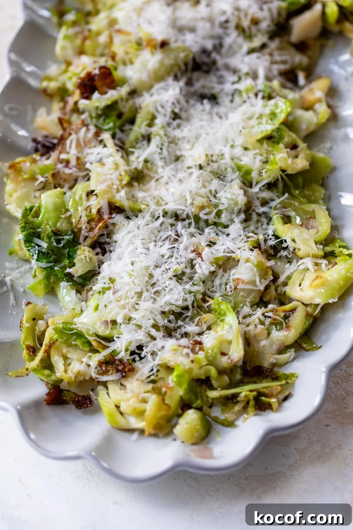 shaved brussels sprouts topped with shredded cheese on a white serving platter.