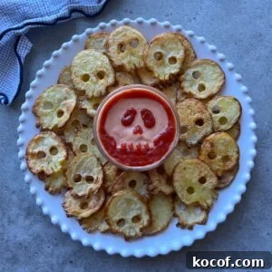 A plate of skull-shaped potato slices arranged around a bowl of dip with a skull face design made from sauce on top.