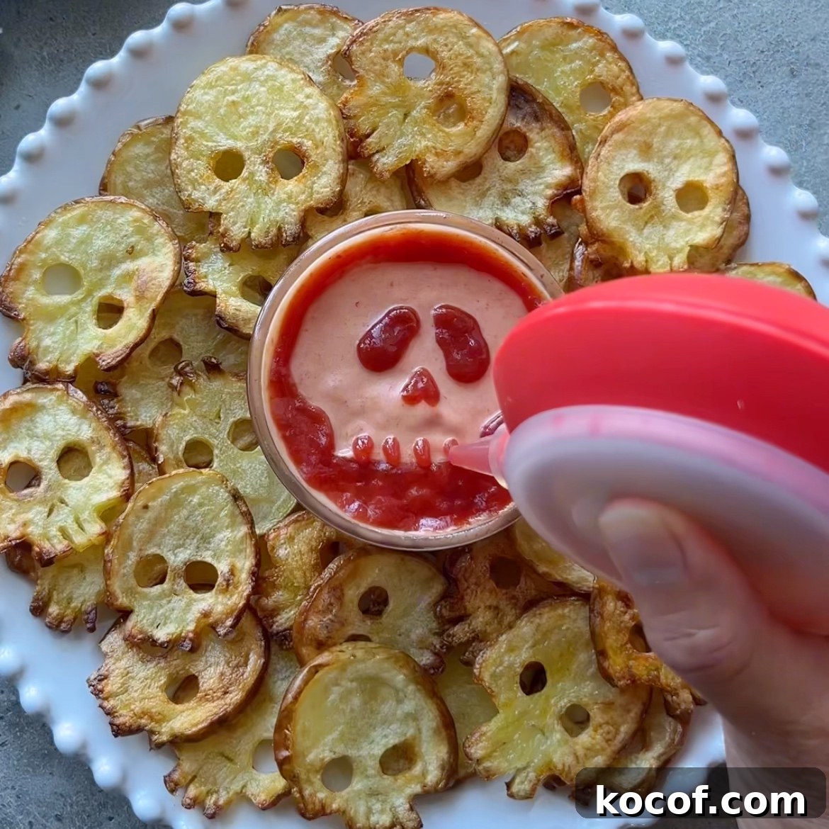 A plate of Halloween Fries shaped like skulls surrounds a bowl of dip decorated with a skull design in ketchup.
