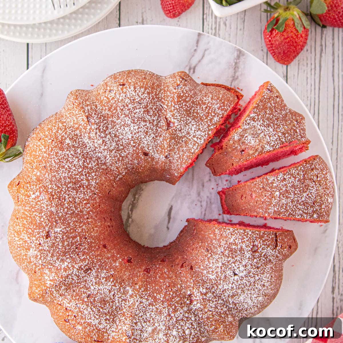 Classic Summer Strawberry Dessert Recipes You’ll Love 7 A marble plate displays a strawberry bundt cake with 2 slices cut to show the red cake color.