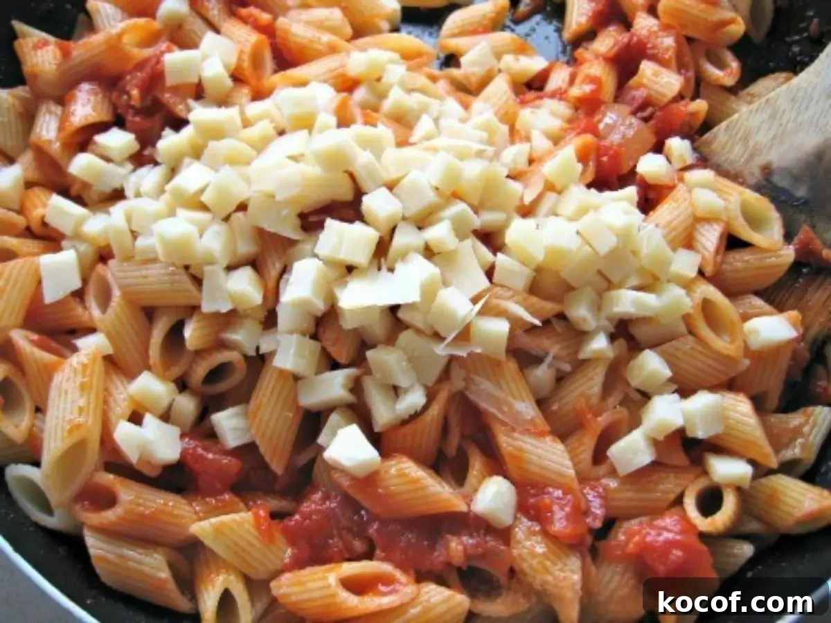 Mezze penne tossed in tomato sauce with cubes of provolone melting over the top in a wide pan.