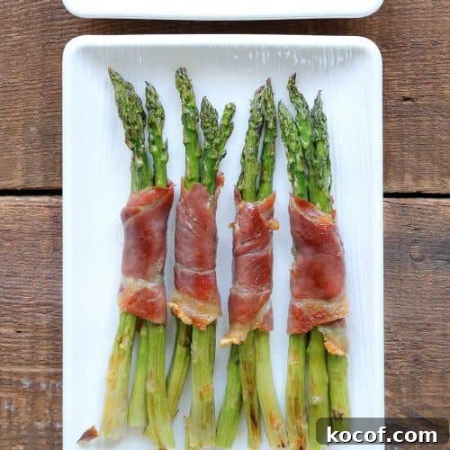 prosciutto wrapped asparagus on a white platter.