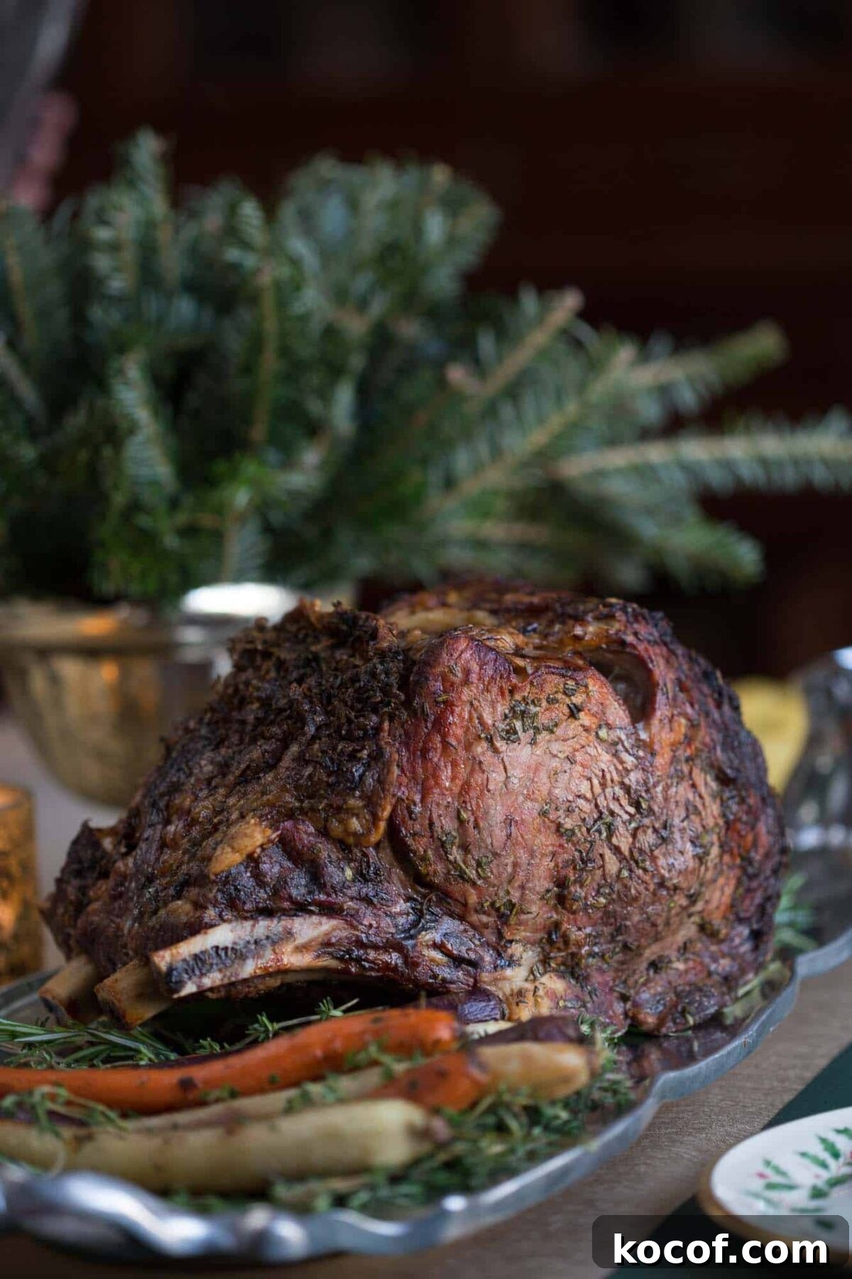 Herb-Roasted Prime Rib Roast: Tender, Juicy Holiday Recipe 4 prime rib on a serving platter with roasted carrots, with greenery in the background.