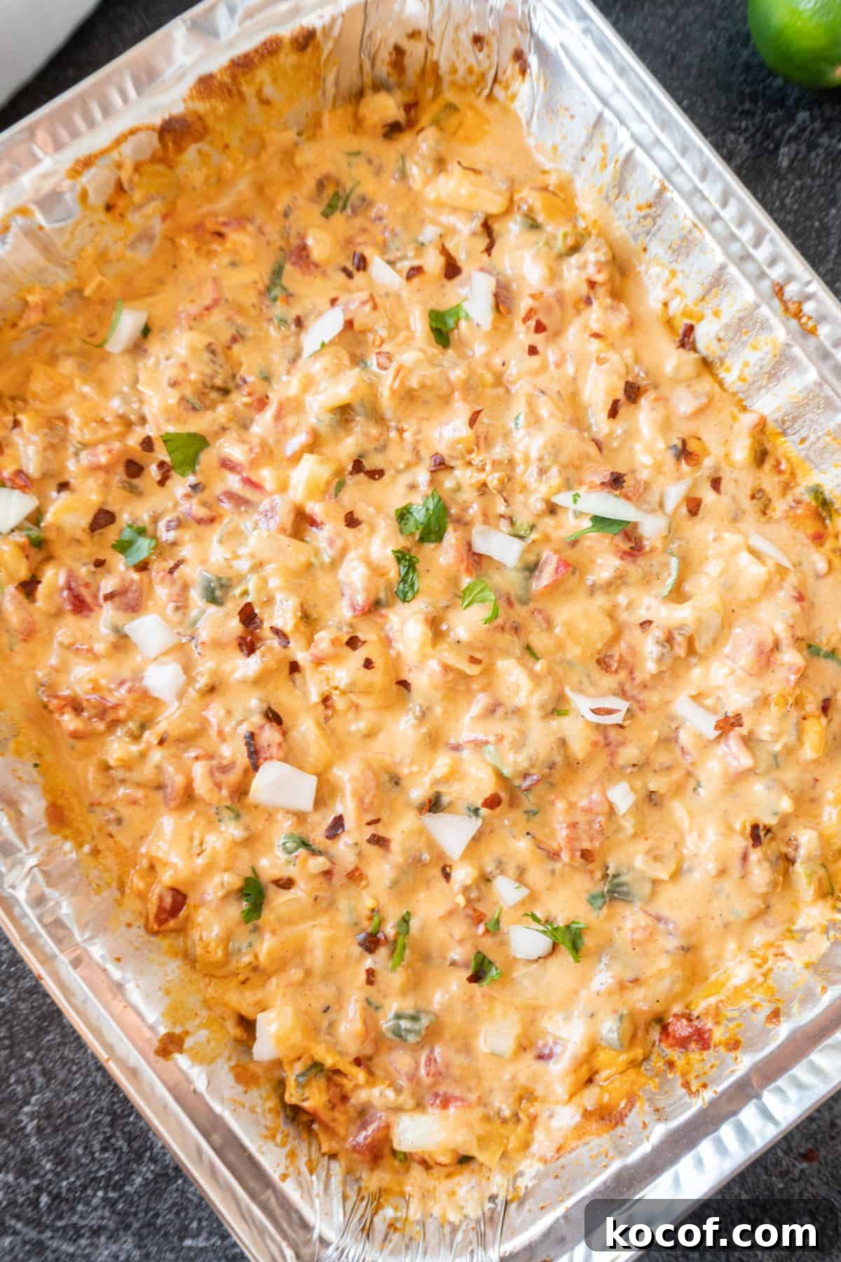 Smoked Queso in an aluminum pan sprinkled with fresh onion and cilantro.