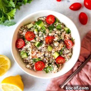 Salmon quinoa salad in a white bowl surrounded by cherry tomatoes, fresh parsley, and a cut lemon.