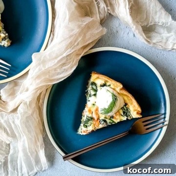 A slice of smoked salmon and spinach quiche on a teal plate with a copper fork.