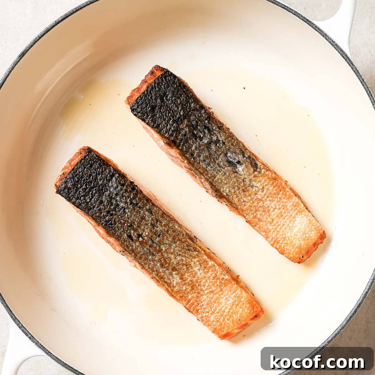 Two pieces of salmon being cooked in a pan skin-side up.