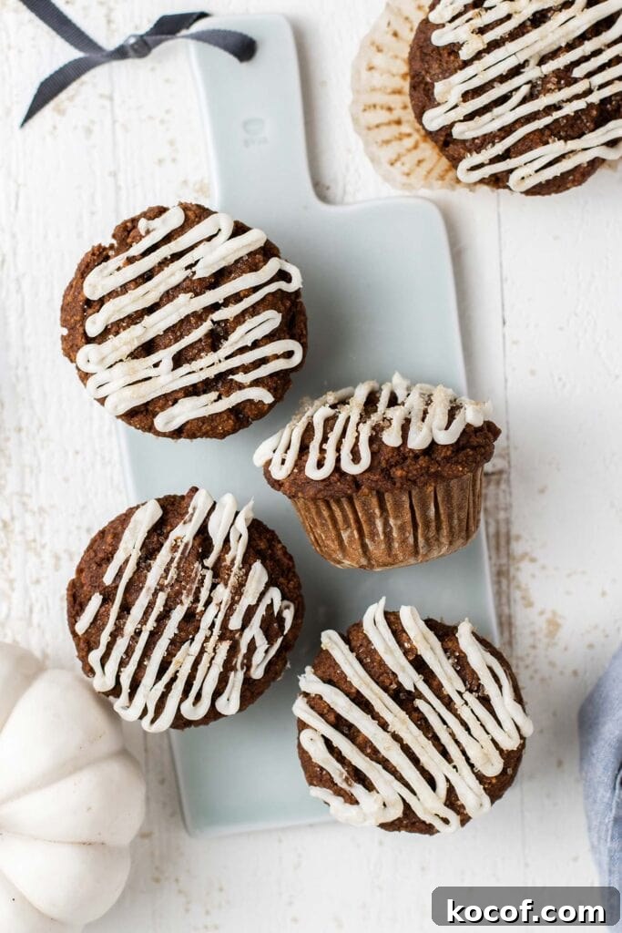 Pumpkin gingerbread muffins on a blue cutting board drizzled with cream cheese glaze.