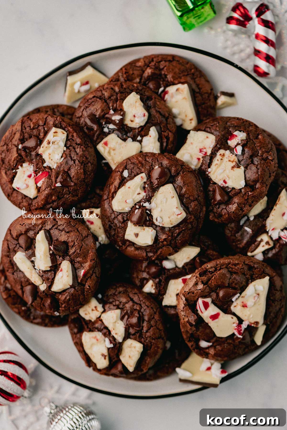 Plate full of peppermint bark brownie crinkle cookies with ornaments around the plate | © Beyond the Buter®
