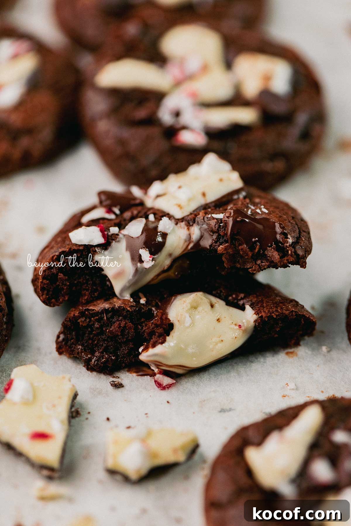 A split peppermint bark brownie crinkle cookie on a parchment paper lined baking sheet | © Beyond the Buter®