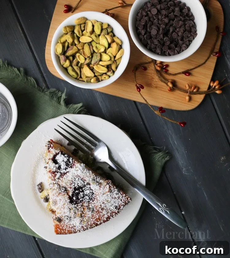 Cannoli-Inspired Breakfast Cake with Ricotta and Chocolate Chips 7 Overhead view of a slice of Easy Cannoli Breakfast Cake next to bowls of pistachios and chocolate chips by The Merchant Baker
