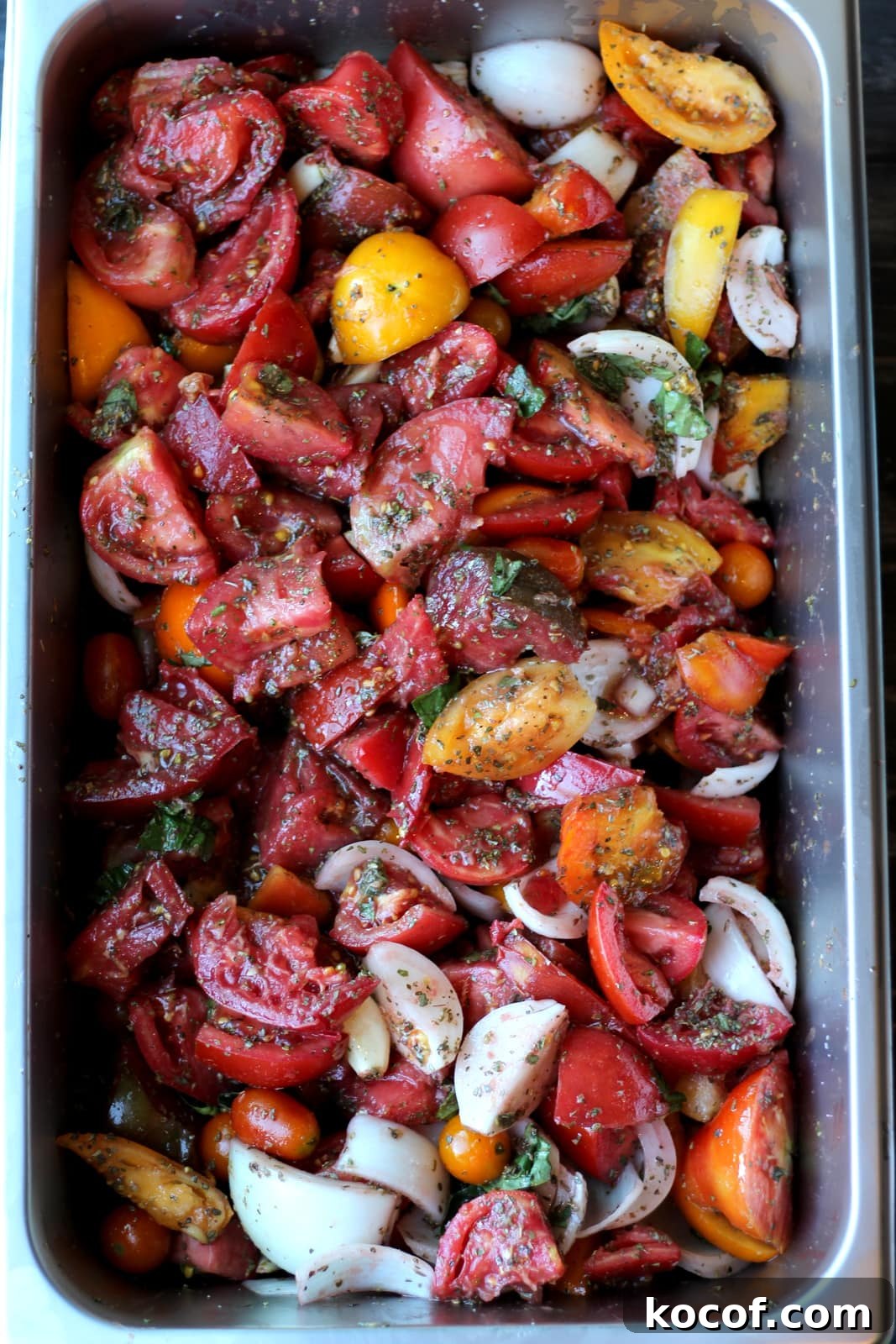 Large aluminum pan filled with fresh tomatoes, herbs and onion.