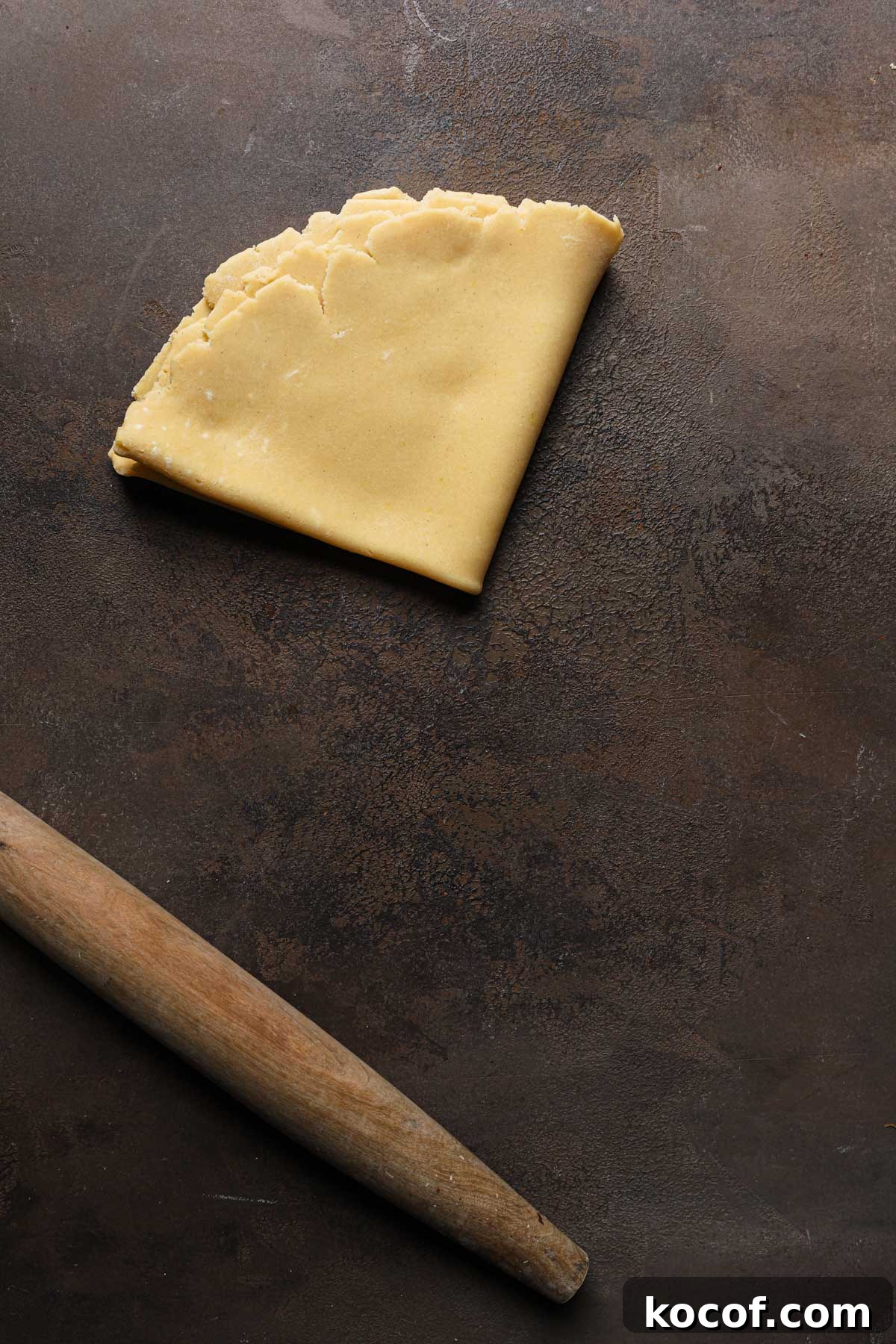 Italian Pasta Frolla Shortcrust Recipe for Tarts & Cookies 15 Rolled dough folded over itself in a triangle shape next to a rolling pin.