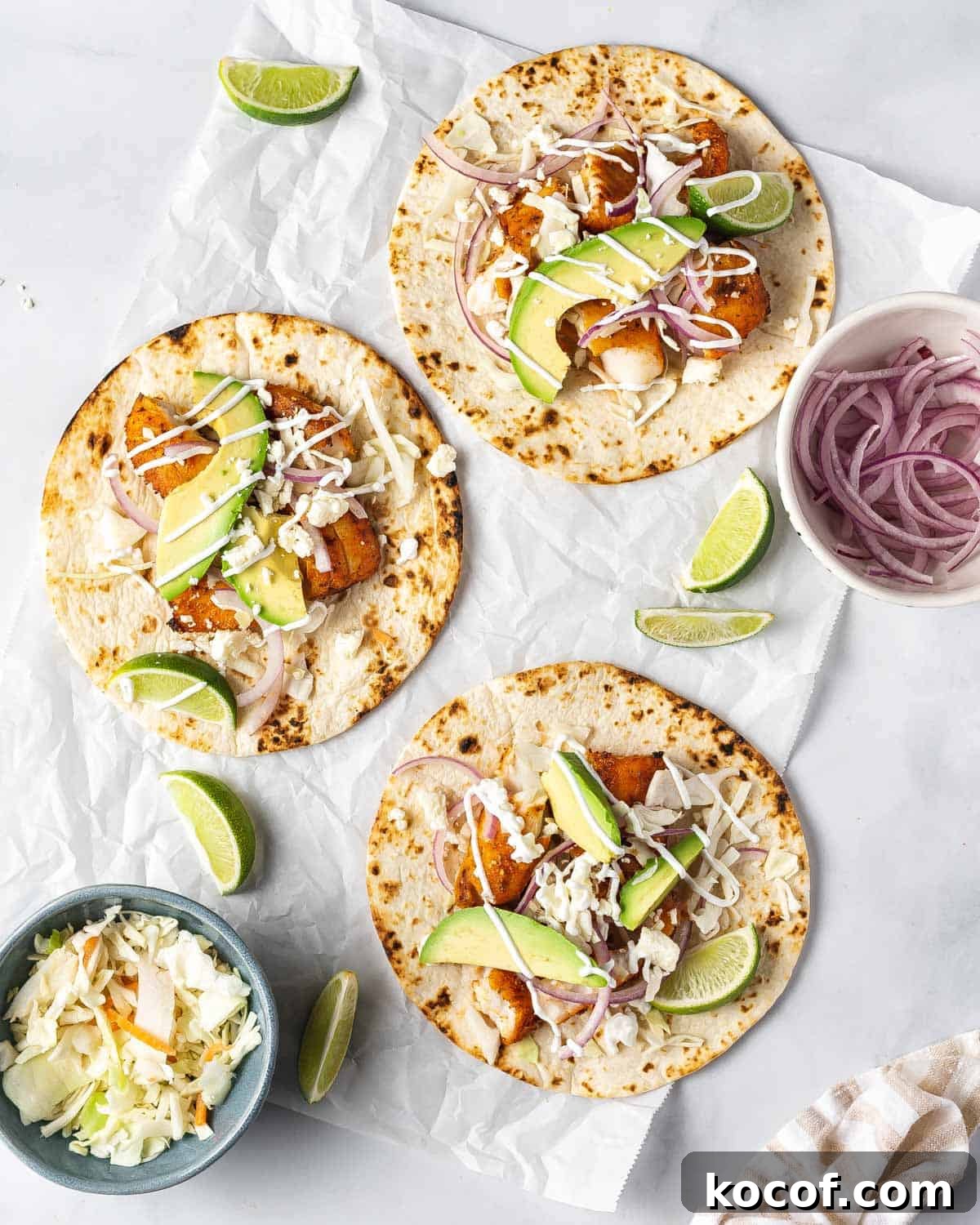 Three air fryer fish tacos with toppings scattered around.