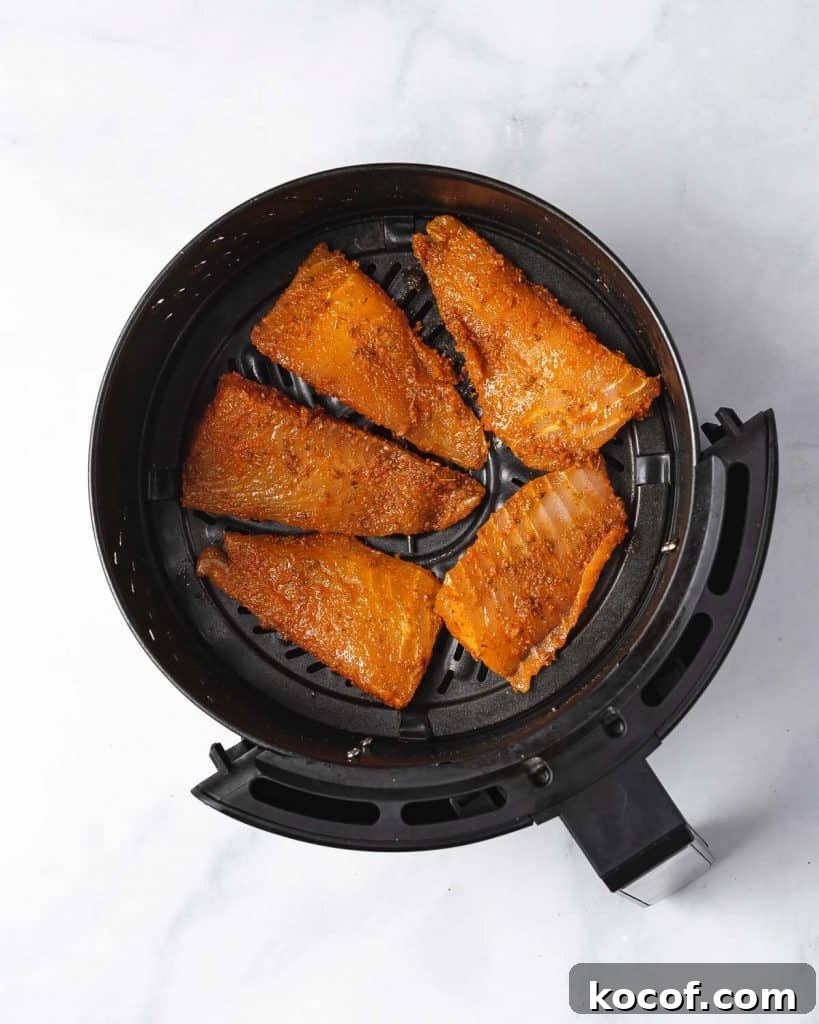 Air fryer basket with seasoned fish fillets.