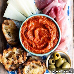 A cropped image of Ajvar, a red pepper dip in a blue bowl surrounded by antipasti.