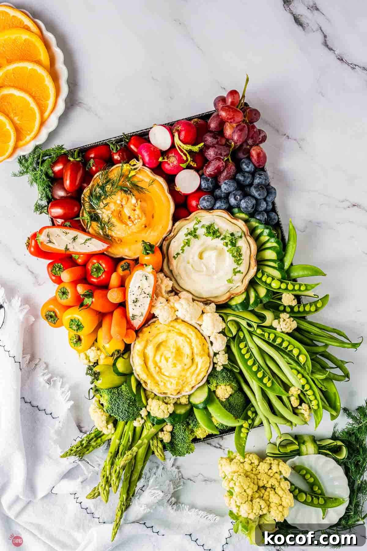 Colorful vegetable and fruit platter with cherry tomatoes, grapes, radishes, and sliced cucumbers.