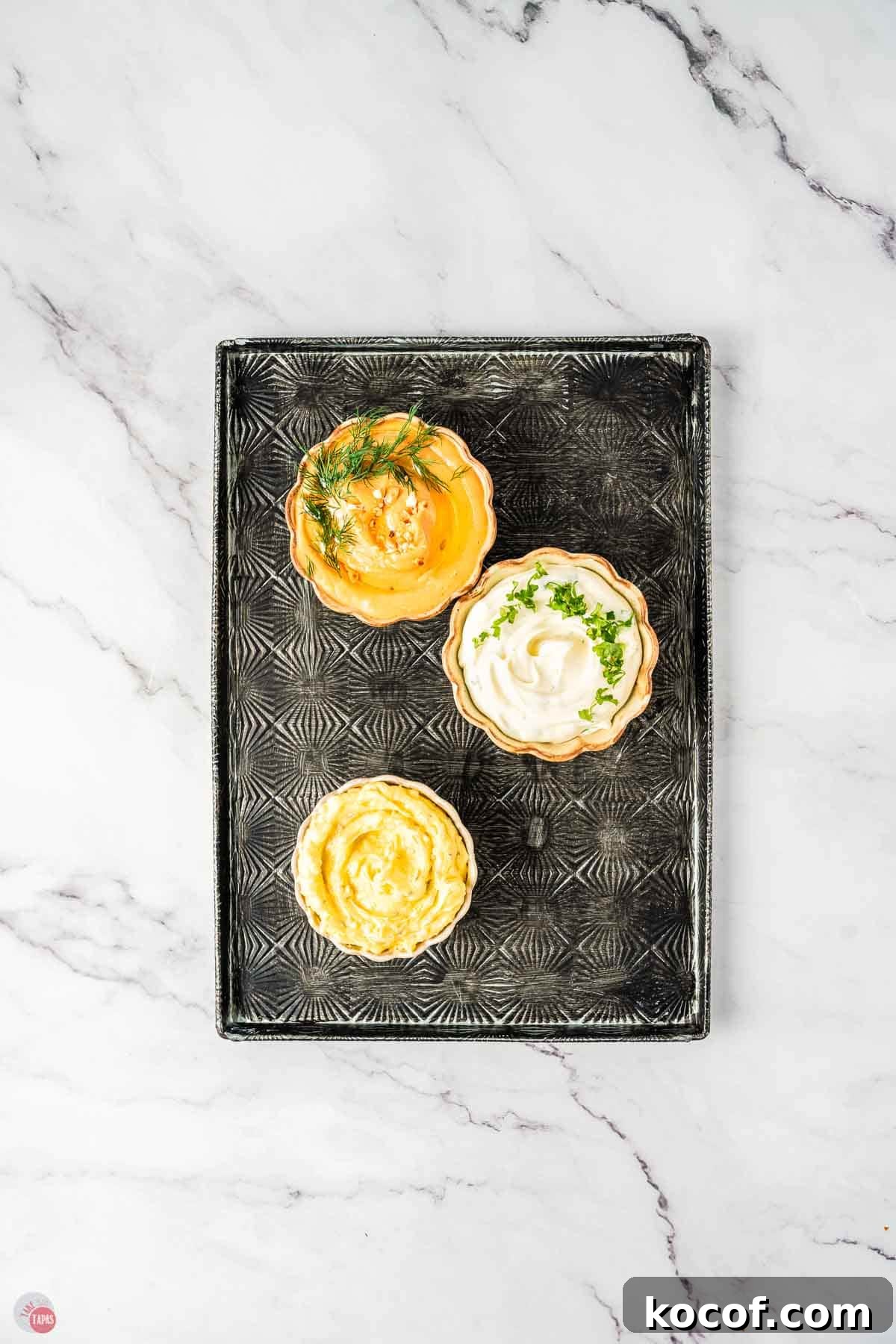 Assorted dips in bowls on a black textured serving tray.