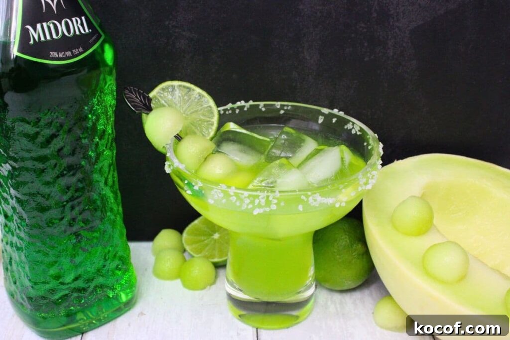 midori margarita next to the bottle and a half of a fresh cut melon