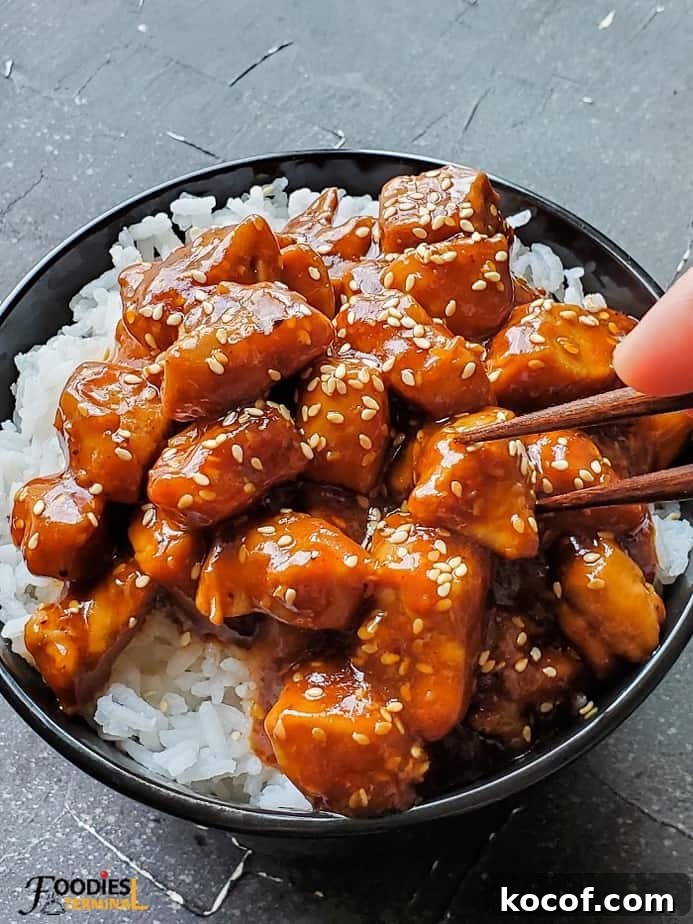 Instant Pot sesame chicken on rice in a black bowl with chopsticks